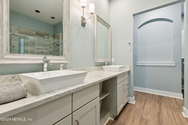 bathroom featuring double vanity, a stall shower, a sink, and wood finished floors