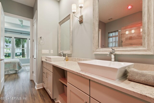 ensuite bathroom with double vanity, ensuite bath, a sink, and wood finished floors