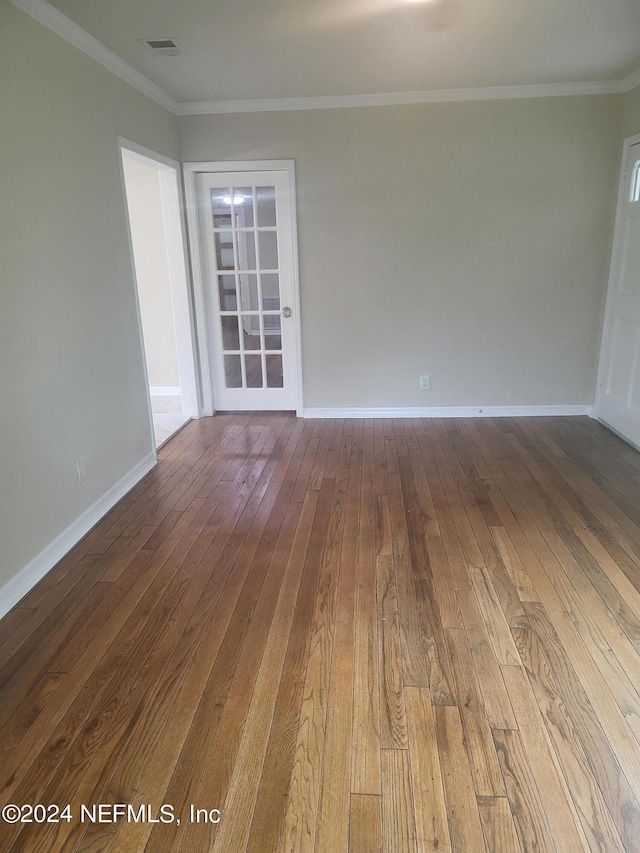 empty room with ornamental molding, visible vents, dark wood finished floors, and baseboards