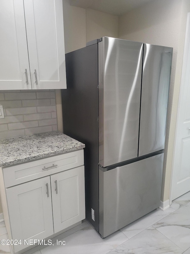 kitchen with stainless steel refrigerator, white cabinetry, light stone countertops, and decorative backsplash