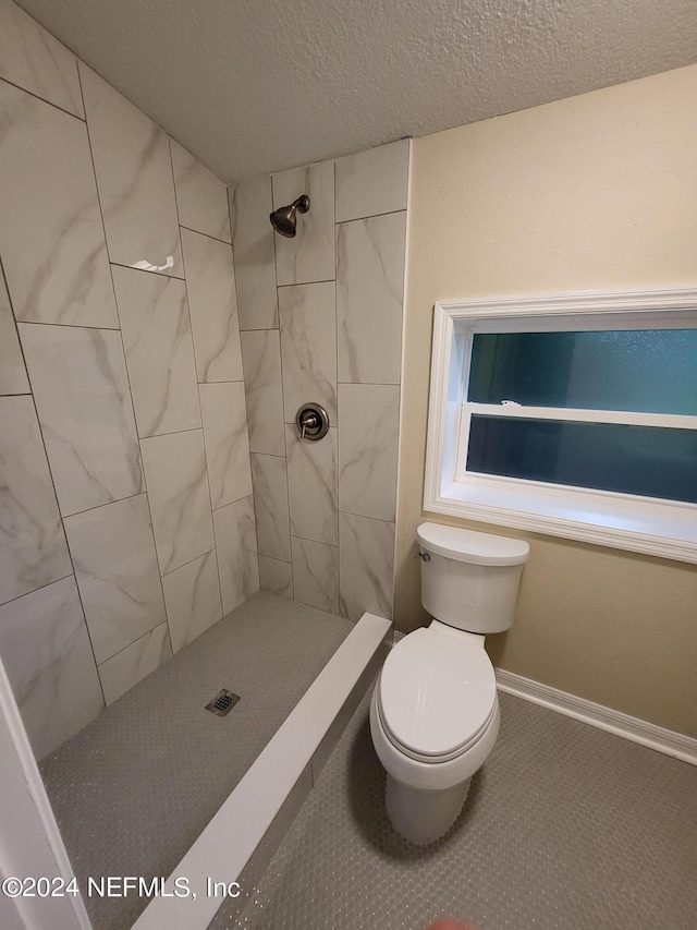 full bath with a textured ceiling, a shower stall, toilet, and baseboards