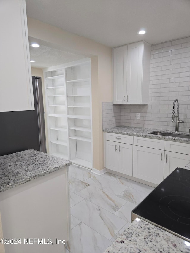 kitchen featuring light stone counters, range with electric stovetop, sink, and white cabinets