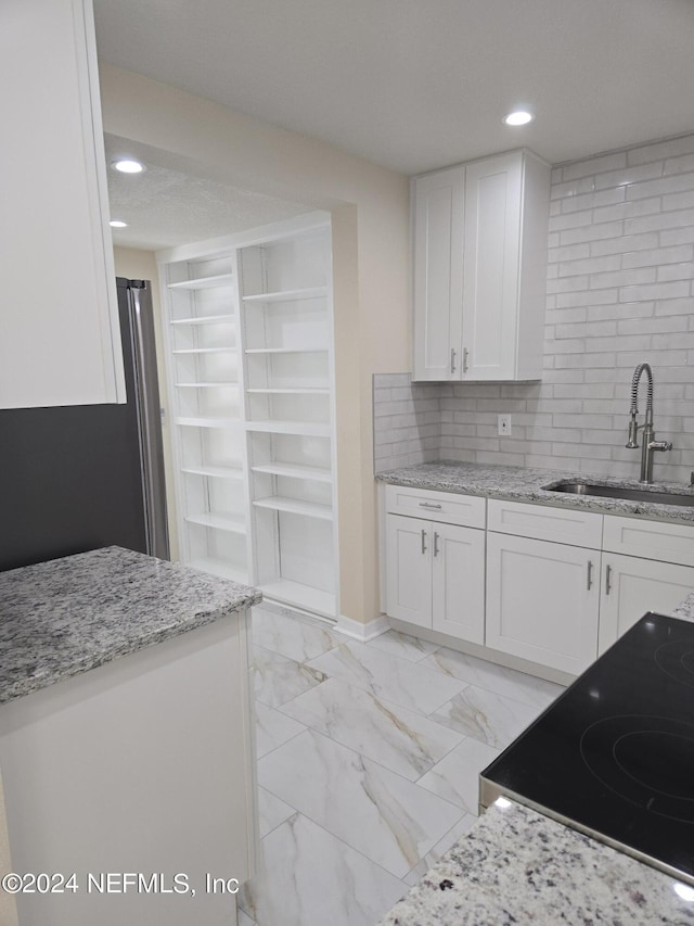 kitchen with light stone counters, marble finish floor, white cabinets, a sink, and range