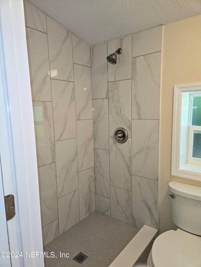 bathroom with a tile shower, toilet, and a textured ceiling