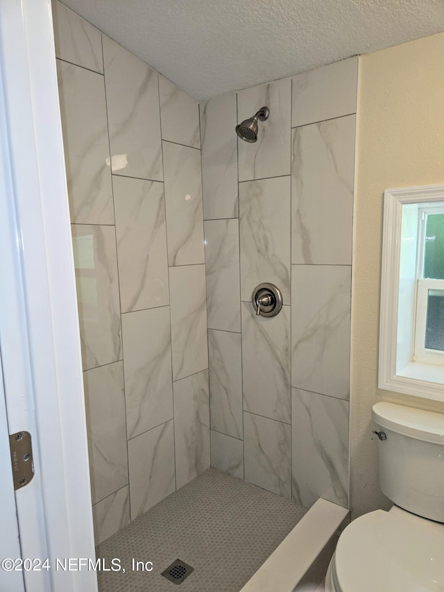 full bath featuring a textured ceiling, tiled shower, and toilet