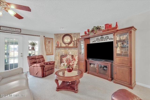 living room with french doors, a textured ceiling, carpet floors, ceiling fan, and a stone fireplace