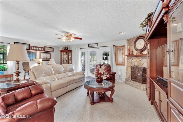 carpeted living room with a stone fireplace, a textured ceiling, ceiling fan, and french doors