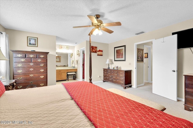 bedroom with a textured ceiling, connected bathroom, light colored carpet, and ceiling fan