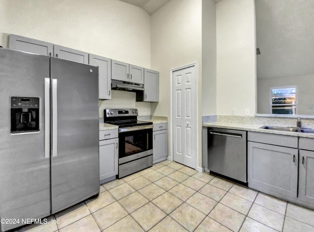 kitchen with a high ceiling, light tile patterned flooring, appliances with stainless steel finishes, and gray cabinetry