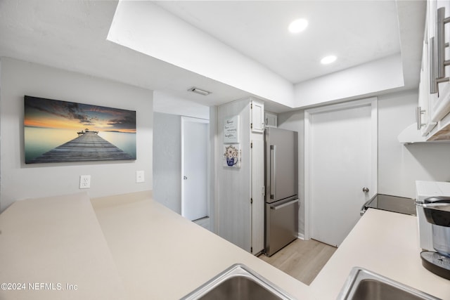 kitchen featuring stainless steel fridge, light wood-type flooring, and white cabinetry