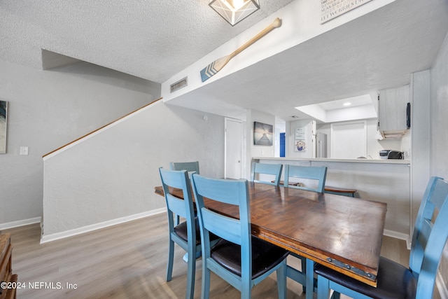 dining space with a raised ceiling, a textured ceiling, and light wood-type flooring