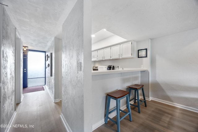 kitchen with a kitchen bar, kitchen peninsula, white cabinetry, and wood-type flooring