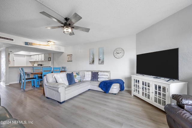 living room featuring ceiling fan, light wood-type flooring, and a textured ceiling