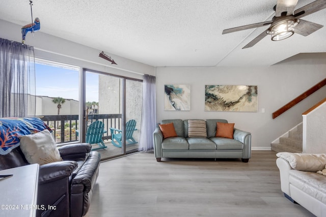 living room with ceiling fan, light wood-type flooring, and a textured ceiling