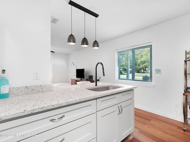 kitchen featuring white cabinetry, light stone countertops, light wood-type flooring, decorative light fixtures, and sink