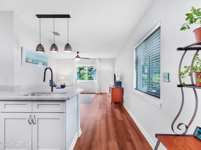 kitchen with sink, dark hardwood / wood-style flooring, white cabinetry, decorative light fixtures, and light stone counters