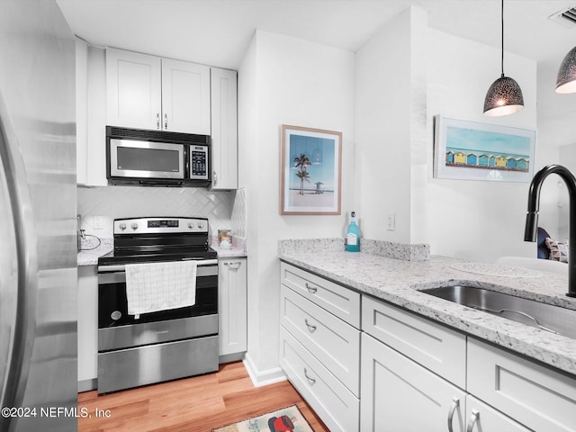 kitchen with appliances with stainless steel finishes, sink, light hardwood / wood-style floors, decorative light fixtures, and white cabinets