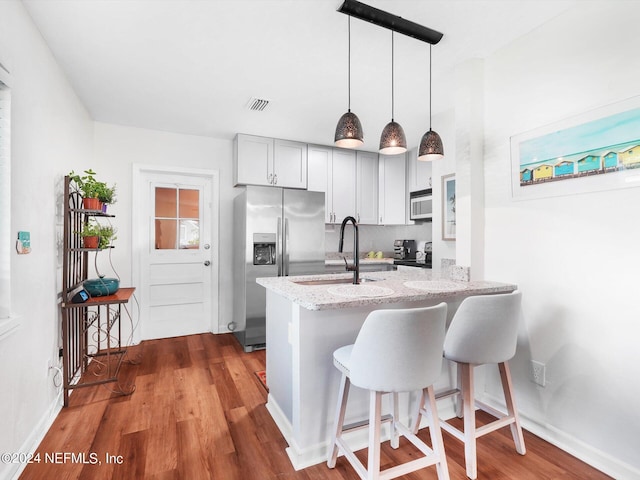 kitchen featuring kitchen peninsula, hanging light fixtures, hardwood / wood-style floors, light stone counters, and stainless steel refrigerator with ice dispenser