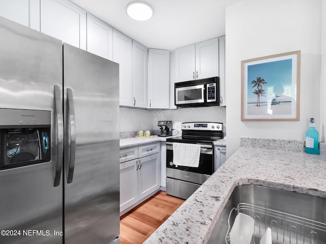 kitchen with decorative backsplash, appliances with stainless steel finishes, light stone countertops, light hardwood / wood-style floors, and sink