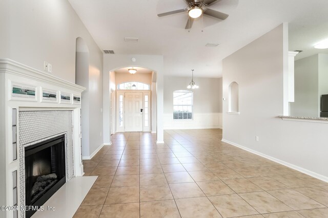 unfurnished living room featuring ceiling fan with notable chandelier, a tiled fireplace, and light tile patterned floors