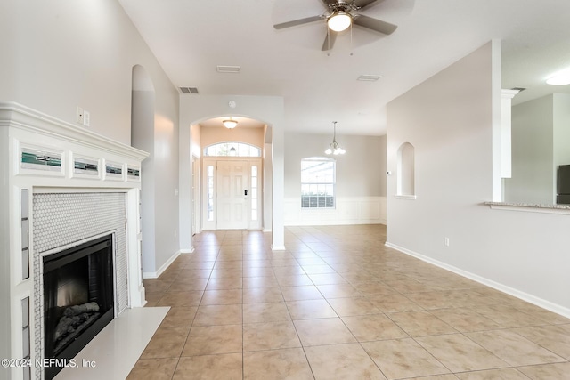 unfurnished living room with a tiled fireplace, light tile patterned flooring, and ceiling fan