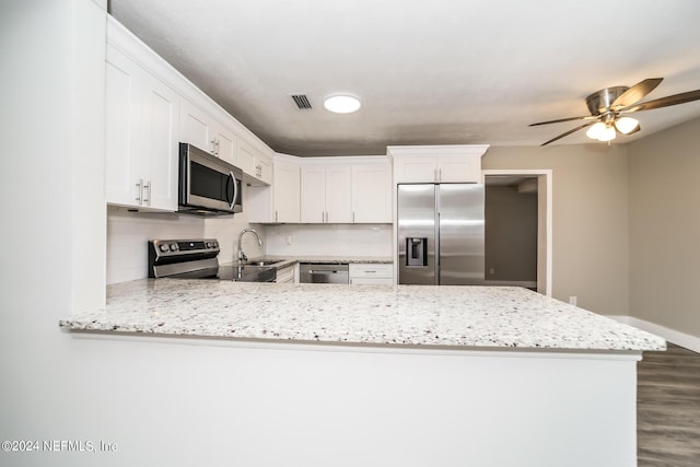 kitchen with stainless steel appliances, kitchen peninsula, light stone countertops, and white cabinets