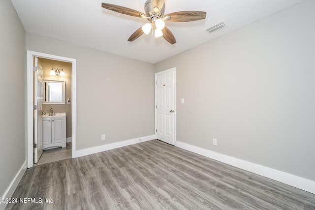 unfurnished bedroom with ceiling fan, wood-type flooring, ensuite bathroom, and sink