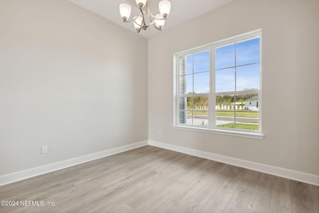 spare room featuring a chandelier, light hardwood / wood-style flooring, and plenty of natural light