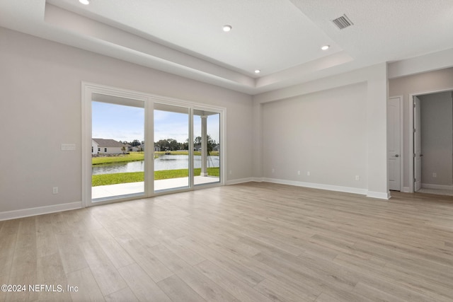 spare room featuring light wood-type flooring, a raised ceiling, a water view, and a textured ceiling