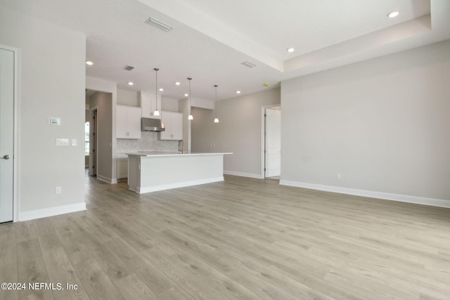 unfurnished living room featuring sink, a tray ceiling, and light hardwood / wood-style floors