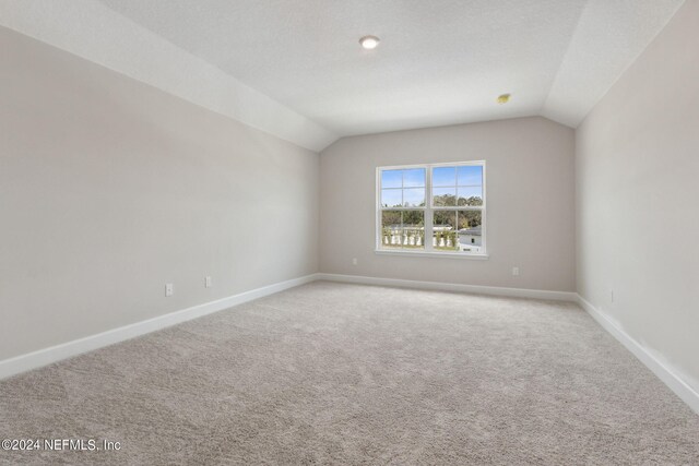 carpeted empty room with lofted ceiling