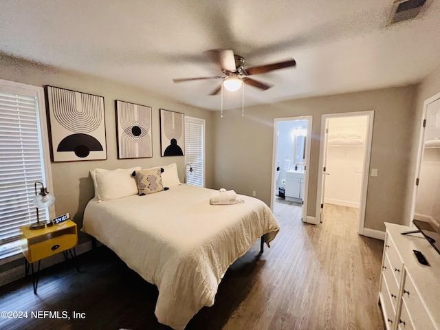 bedroom with ceiling fan, ensuite bathroom, light hardwood / wood-style floors, a textured ceiling, and a spacious closet