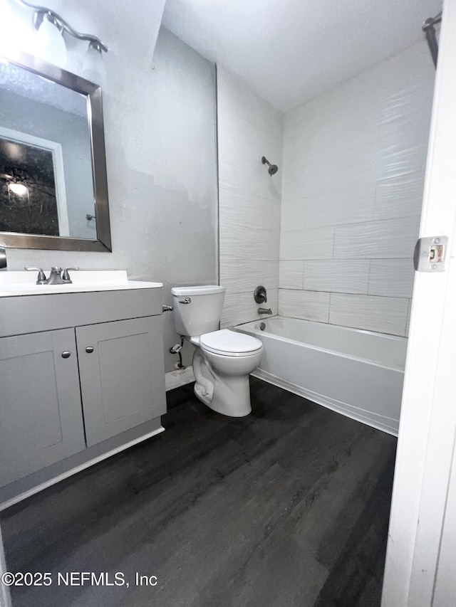 full bathroom with hardwood / wood-style flooring, tiled shower / bath, vanity, and toilet