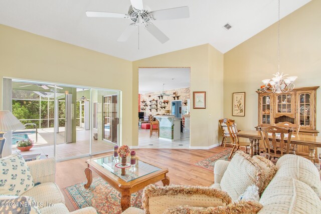 living room with ceiling fan with notable chandelier, wood-type flooring, and high vaulted ceiling