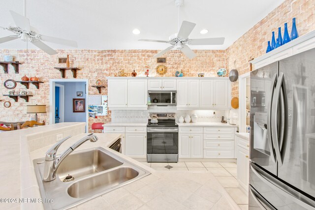 kitchen featuring white cabinets, ceiling fan, stainless steel appliances, brick wall, and sink