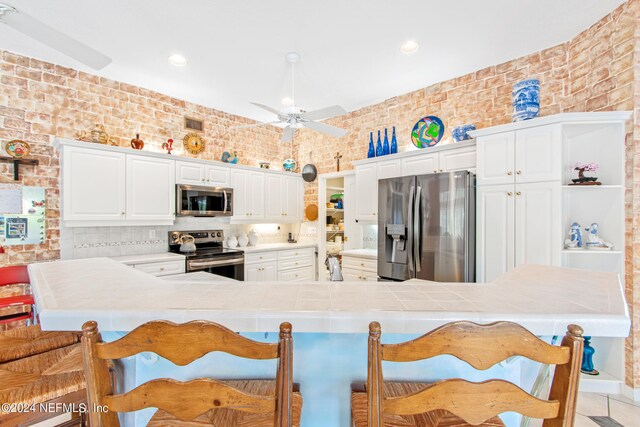 kitchen featuring kitchen peninsula, appliances with stainless steel finishes, brick wall, and white cabinets