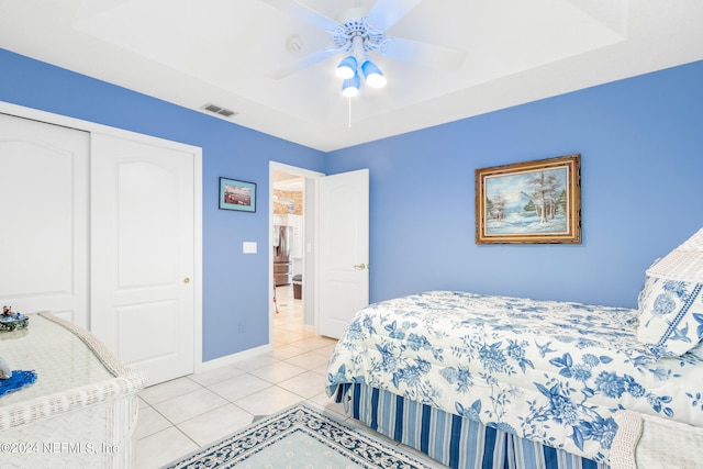 bedroom with a raised ceiling, a closet, light tile patterned floors, and ceiling fan