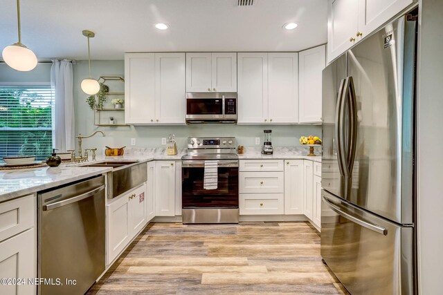 kitchen with white cabinetry, light hardwood / wood-style floors, hanging light fixtures, and appliances with stainless steel finishes