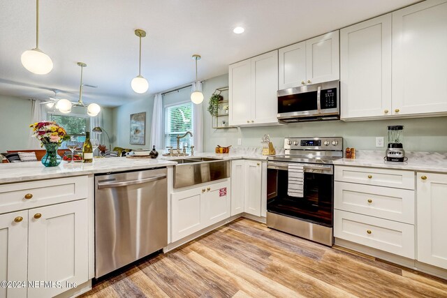 kitchen featuring appliances with stainless steel finishes, decorative light fixtures, white cabinets, and light wood-type flooring