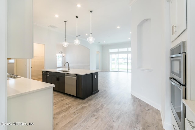 kitchen with a kitchen island with sink, sink, decorative light fixtures, white cabinetry, and stainless steel appliances