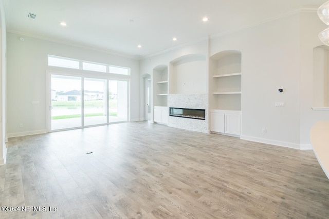 unfurnished living room with built in shelves, crown molding, a fireplace, and light hardwood / wood-style flooring