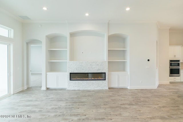 unfurnished living room featuring crown molding, a fireplace, light hardwood / wood-style floors, and built in features