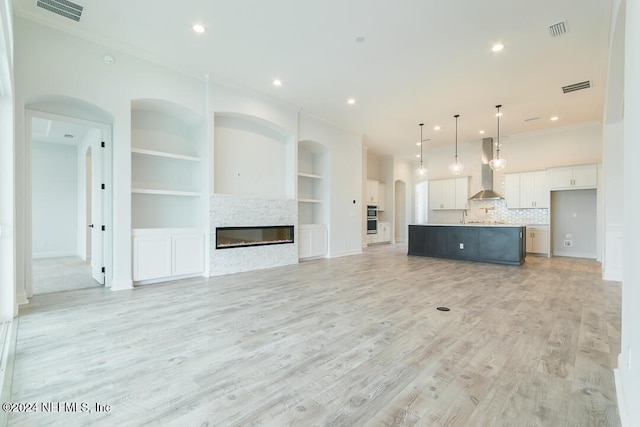 unfurnished living room with built in shelves, a stone fireplace, light wood-type flooring, and ornamental molding