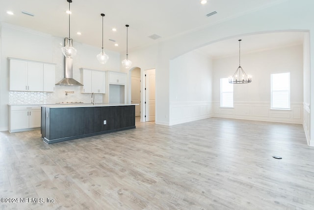 kitchen with hanging light fixtures, light wood-type flooring, an island with sink, a notable chandelier, and white cabinetry