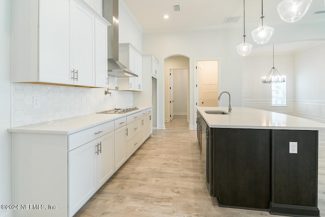 kitchen with wall chimney range hood, sink, hanging light fixtures, light hardwood / wood-style flooring, and white cabinetry