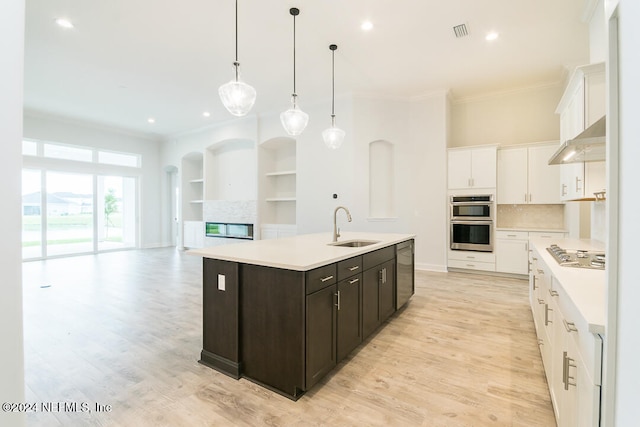 kitchen featuring a kitchen island with sink, exhaust hood, sink, hanging light fixtures, and dark brown cabinets