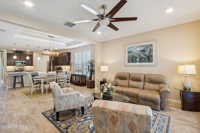 living room featuring light hardwood / wood-style floors, ceiling fan with notable chandelier, and a raised ceiling