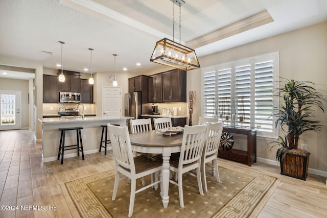 dining area with a notable chandelier, a textured ceiling, light hardwood / wood-style floors, a raised ceiling, and sink