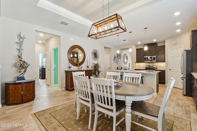 dining area with sink, light wood-type flooring, a raised ceiling, and a notable chandelier