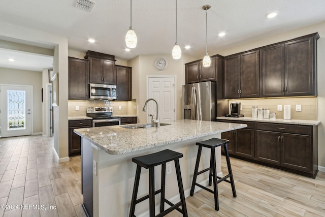 kitchen featuring tasteful backsplash, stainless steel appliances, pendant lighting, a kitchen island with sink, and a kitchen breakfast bar